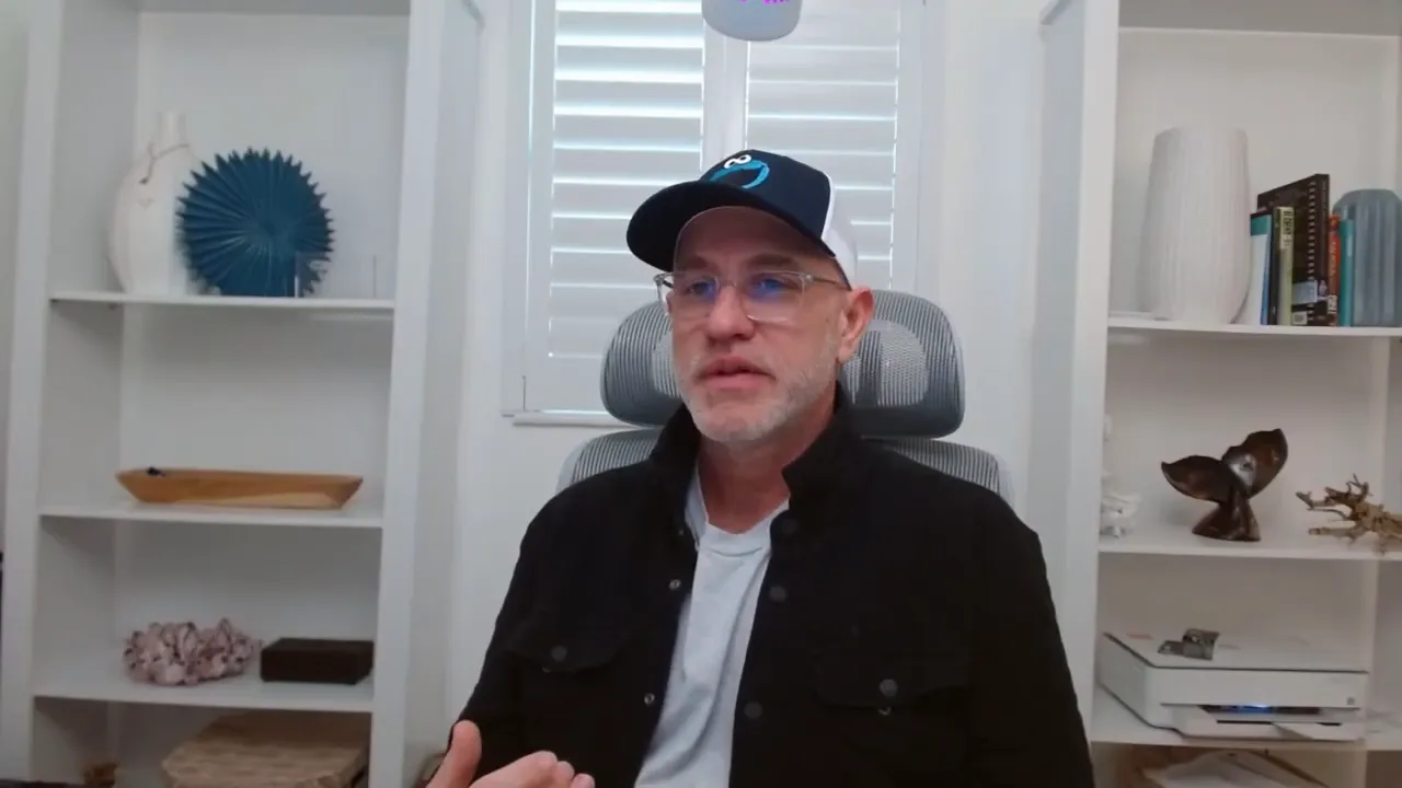Presenter touching his forehead while speaking, bookshelf in the background